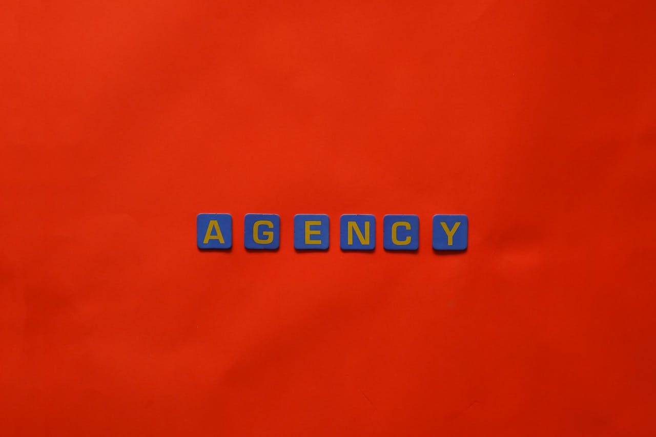 Blue letter tiles spelling AGENCY on a vibrant red background, ideal for creative promotion.
